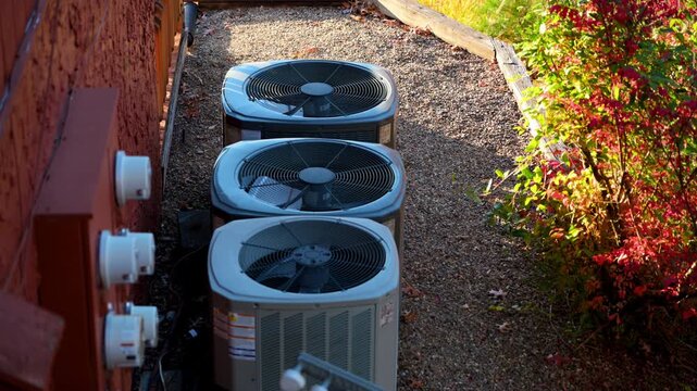 Home HVAC Air Conditioner system working outside the house. Bright autumn sunny day with beautiful foliage. Bushes leaves moving on the wind