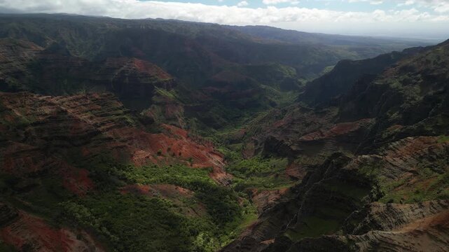 Aerial drone cinematic panorama flying over vast waimea canyon revealing deep valleys layered red cliffs lush green ridges and dramatic geological formations in kauai hawaii
