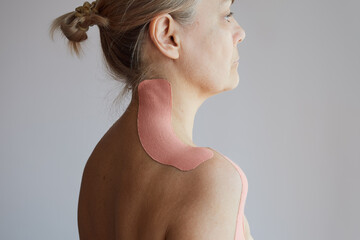 Profile view of a woman wearing kinesiology tape on her neck and shoulders for muscle support and pain relief.