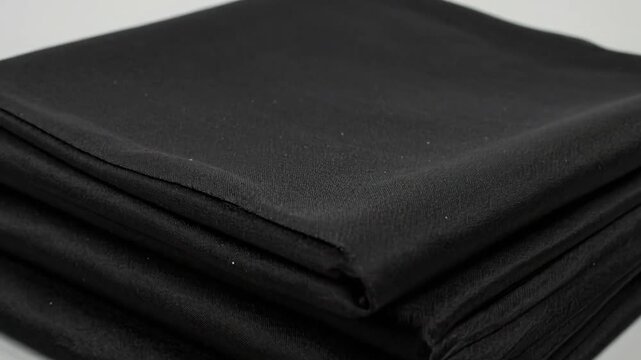 A stack of neatly folded, dark, black fabric squares. Smooth texture with soft folds