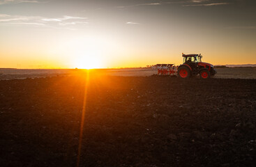 Fototapeta premium Tractor plowing field the land at sunset