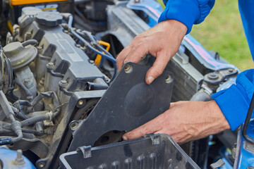 A mechanic removes a plastic timing belt cover, A mechanic's hands service an engine, the timing cover is removed