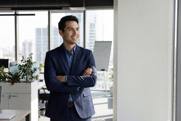  Corporate portrait of European confident student, trade manager businessman standing crossed arms in office. Young latin hispanic specialist business man employee smiling dreaming away. Copy space 