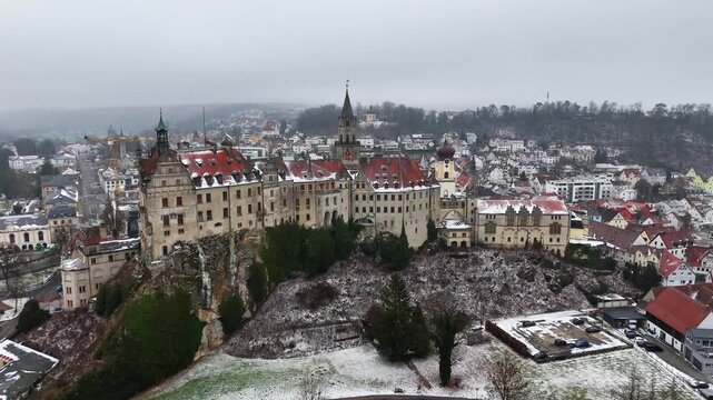 Sigmaringen castle stands on a hilltop as snow covers rooftops in an urban town. The scene fits travel tourism editorial documentary and lifestyle projects focused on European history