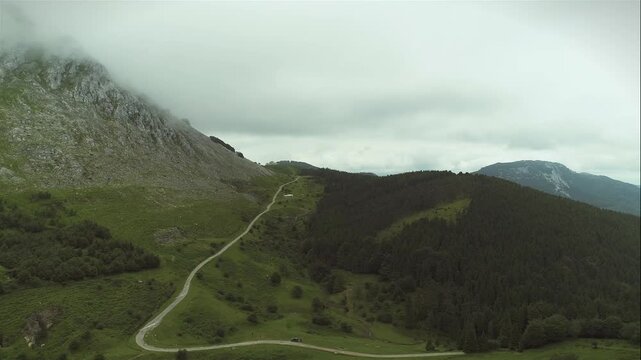 Rolling mountain ridges with narrow trail and patchy grass under low cloud cover and muted light