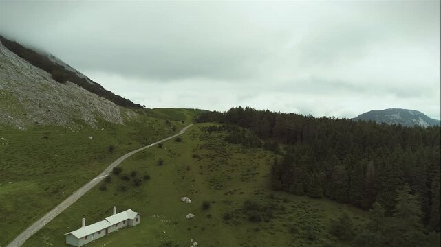 Winding mountain road cuts through grassy slopes beneath heavy clouds in remote highland terrain