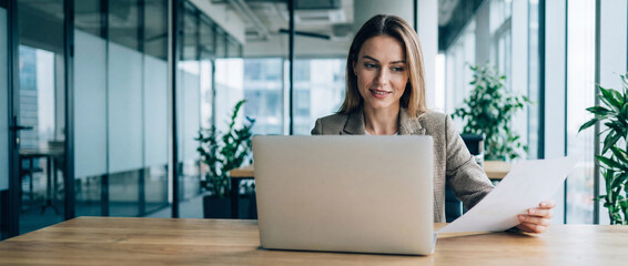 Focused latin business woman accountant working on laptop computer reading financial contract document in office workplace. Mature manager businesswoman specialist doing paperwork using pc. Copy space