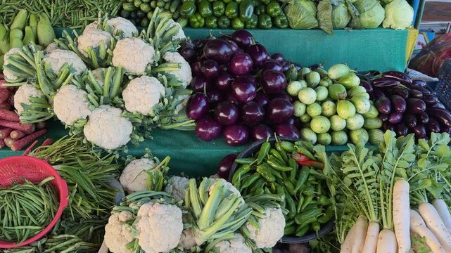 Tracking shot across colorful vegetable market display with cauliflower brinjal tomatoes chilies and radish neatly stacked, camera gliding to reveal freshness variety and texture