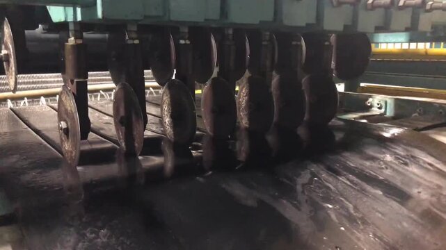 In the rubber factory, rubber sheets exiting the cooling line in  process are being sliced.