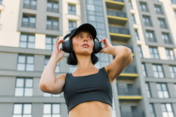 A woman adjusts her headphones while standing outside an apartment building.The beginning of sports...