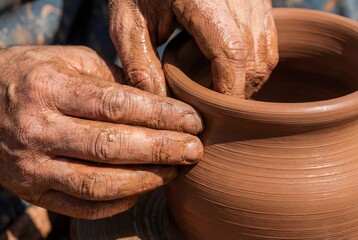 Extreme close-up of a potter's hands shaping clay on a wheel, covered in wet clay