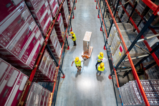 Warehouse workers at work between rows of tall shelving, logistics and distribution center interior, inventory management, teamwork, supply chain and fulfillment operations