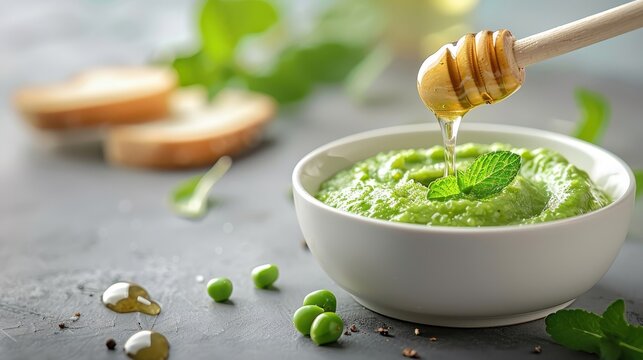 Pea jam spread on warm toasted bread, with fresh mint leaves and a drizzle of honey around.