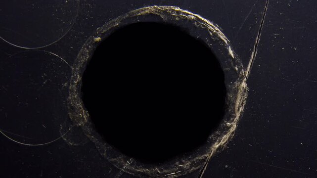 Close up of a hole in a dark surface with rough edges.