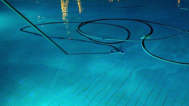 Cleaning the pool bottom with a water vacuum cleaner in the evening. The concept of cleaning pools for hotels, resorts and country houses.