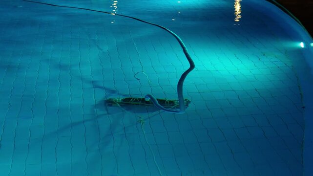 Cleaning the pool bottom with a water vacuum cleaner in the evening. The concept of cleaning pools for hotels, resorts and country houses.