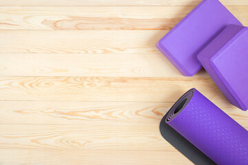 Purple yoga mat and yoga blocks on a light natural wood floor.