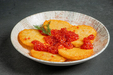 A plate displays golden potato pancakes adorned with bright red caviar and a sprig of dill