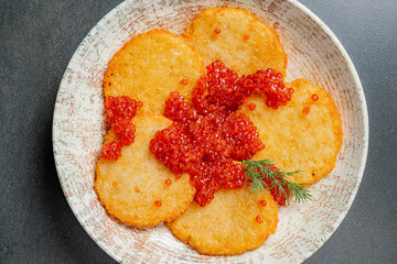 Crispy potato pancakes are garnished with bright red caviar for a delightful dish