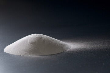 A pile of fine white powder on a dark background with dramatic side lighting
