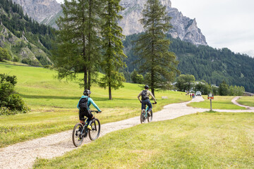 Couple cycling together on a mountain trail surrounded by alpine forest and scenic peaks. Active outdoor adventure for two in summer nature. Sustainable tourism and quality time in the wild.
