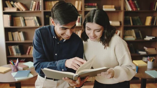 Two students smiling and reading a book together in a library