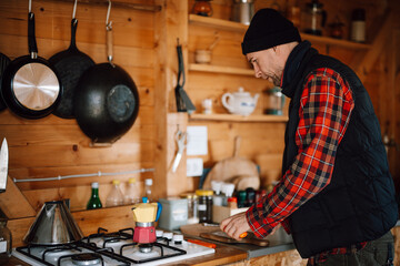 Man prepares food in cabin kitchen with wooden walls