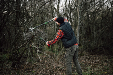 Man uses tools to trim branches in wooded area