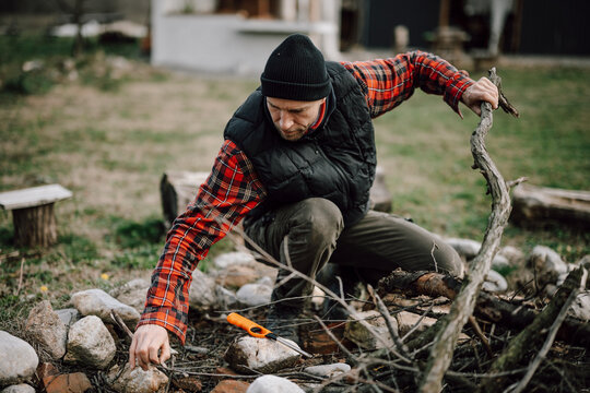 Man collects sticks and stones by a fire pit in a backyard