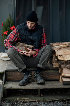 Man sits on stairs holding firewood in front of a stack of logs