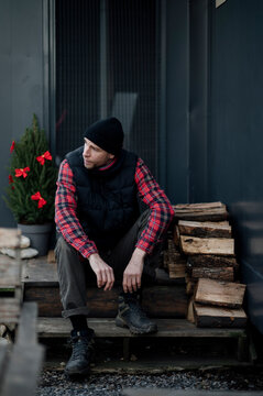 Man sits on steps near firewood and a small plant