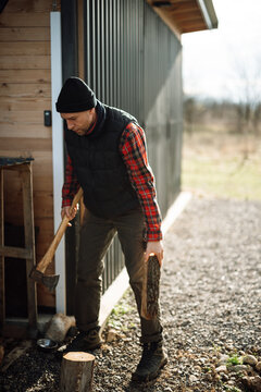 Man splits wood near a wooden cabin