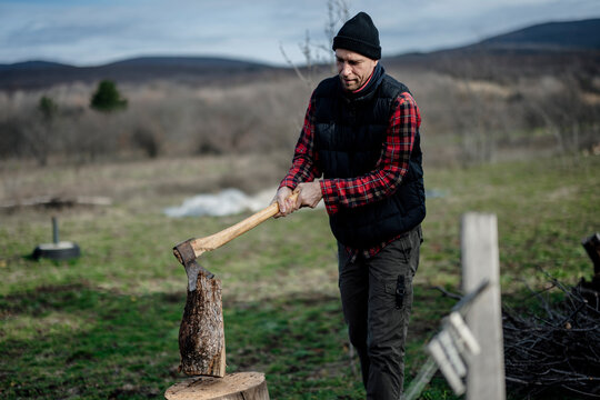 Man splits wood with an axe in an outdoor setting