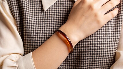 Woman wearing a brown bangle bracelet on checkered fabric background  
