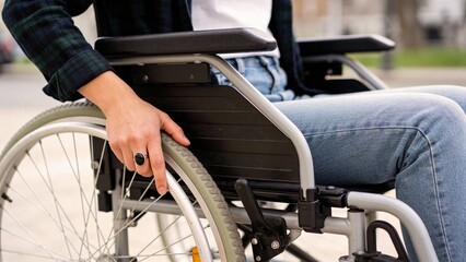 Young woman with disabilities holding wheelchair wheel outdoors  