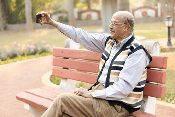 Fototapeta premium Portrait of a joyful senior man taking selfies on smartphone at park
