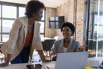 African american women coworkers collaborating in conference room with laptop