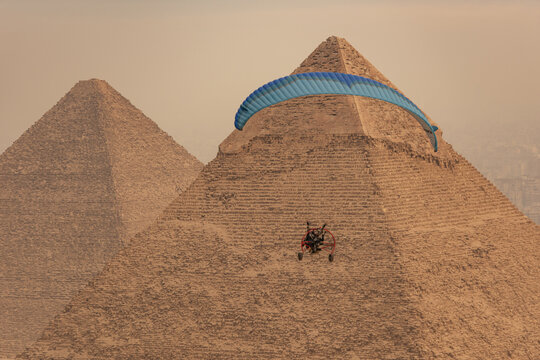 Aerial view of a powered paraglider soars past the ancient pyramids of Giza under a hazy sky, Cairo, Egypt.
