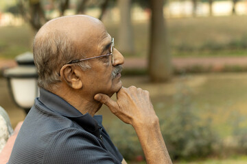 Portrait of a Indian sad, depression, thinking, Upset lonely homeless senior man in garden sitting on bench with with thoughtful face expression