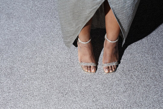 Black woman standing on carpeted floor wearing open toe heels, lower legs and feet visible, adult age group, formal attire implied by dress, feet positioned close together