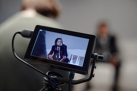 Young Black man singing and gesturing, being filmed with professional camera monitor in foreground, out of focus in background