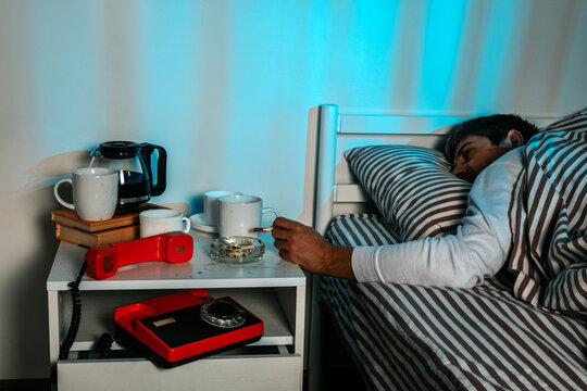 Man smoking and drinking coffee in bed with retro telephone at night
