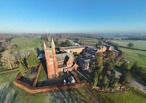 Aerial view of the majestic Rugby School Chapel rises in red brick against a backdrop of green fields and distant trees, Rugby, England, United Kingdom.
