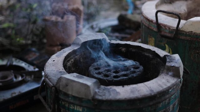 Atmospheric shot of a traditional clay stove with burning honeycomb charcoal briquette and rising blue smoke in a rustic garden