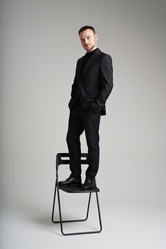 Portrait of man in classic suit standing on chair in minimalist studio