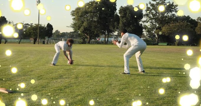 Fielder reaching for ball, partner catching, practicing cricket fielding with yellow bokeh overlay
