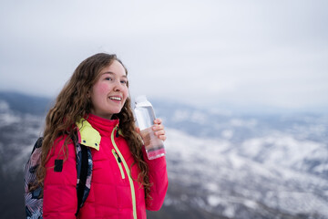 Happy smiling female hiker enjoying water outdoors in winter mountains during daytime hours