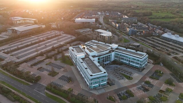 Aerial view of modern office buildings gleaming faintly under the diffused sunlight, surrounded by orderly rows of parking spaces and green spaces, Solihull, England, United Kingdom.