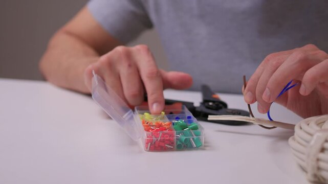 Hands sorting small cable connectors on workbench with assorted colored terminals crimping tool and cable coil visible careful selection of pins tidy workshop tutorial vibe