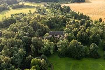 Abandoned building surrounded by dense forest and fields during daylight